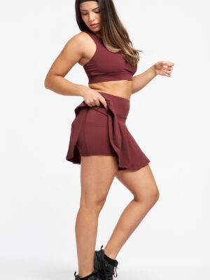 Vista lateral del set Red Vanilla de LatteFit con la modelo levantando la falda para mostrar el short interno.